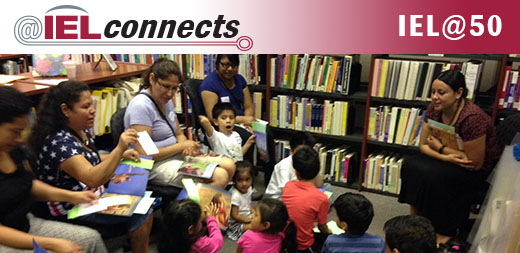 A group of teachers, elementary school children, and theirs their parents gather for reading time in the library.