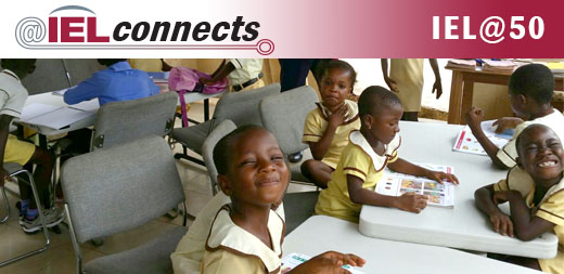 A group of young students in Ghana smile during class, seated in their new chairs from IEL.
