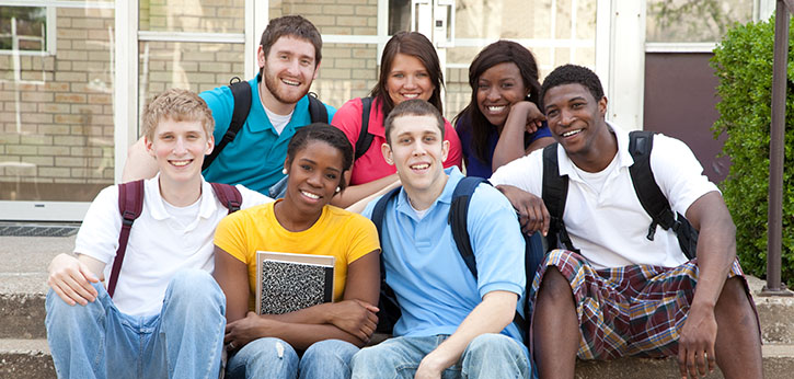 A diverse group of postsecondary students smile outdoors on a college campus.