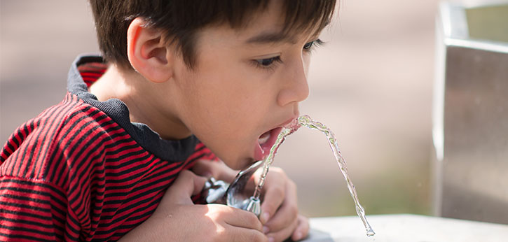 A young boy sips water from a drinking fountain at school.