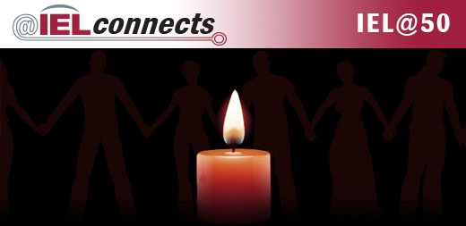 A single candle burning against a black background with shadowed silhouettes of people holding hands