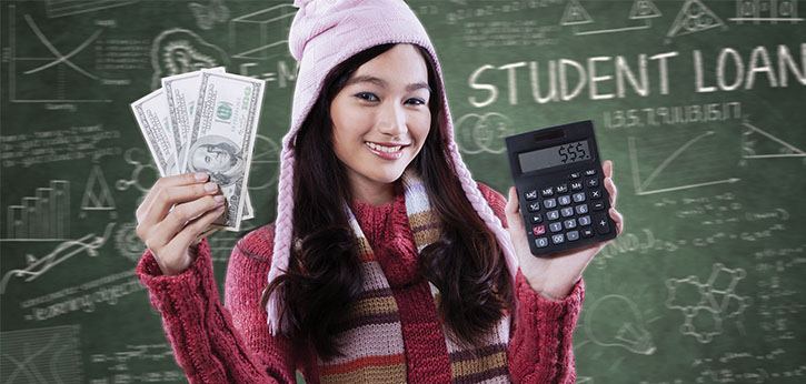 A young woman holds up three hundred-dollar bills in one hand and a calculator with three dollar signs displayed in the other hand. She stands in front of a chalkboard with the words "student loans" and many symbols, calculations, and other text.