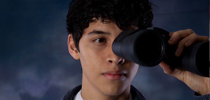 Close up of a male youth looks through a pair of binoculars.