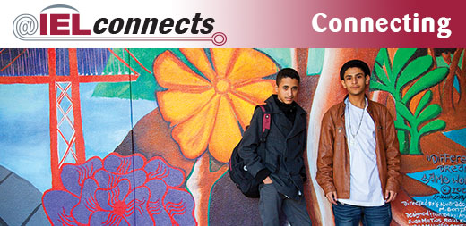IELconnects – Connecting: Two high school students stand in front of an outdoor mural on their community school campus.
