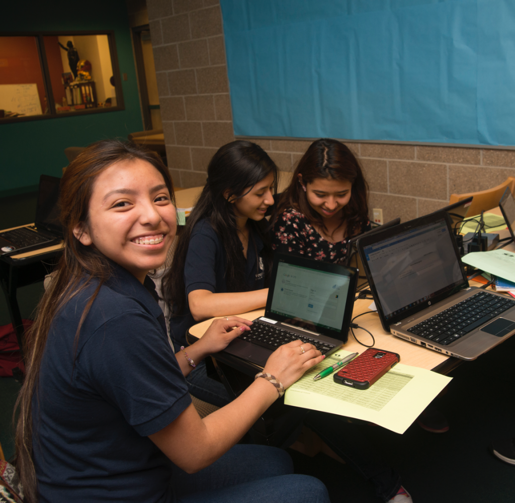 Students sit at a table working on laptops