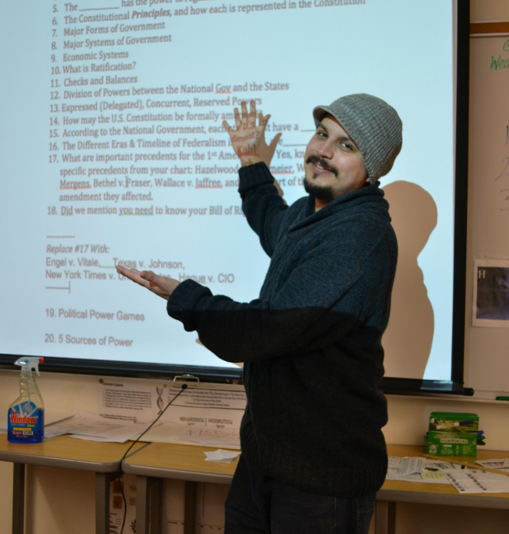Teacher stands in front of a whiteboard pointing at the screen